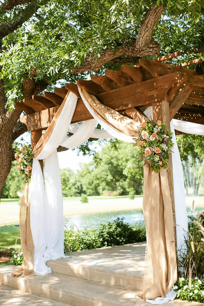 Wooden pergola with flowers and fabric.