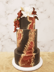 A red, black, and gold wedding cake covered in red and white flowers.