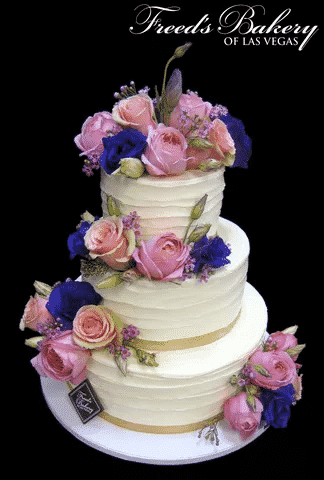 A wedding cake covered in pink and purple roses.